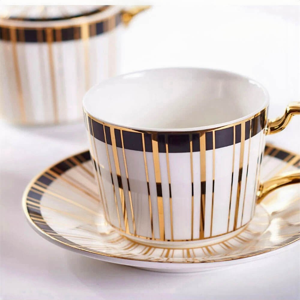 An elegant porcelain tea cup and saucer set with a white base, adorned with vertical black and gold stripes, and a gold-plated handle, creating a luxurious and refined look.