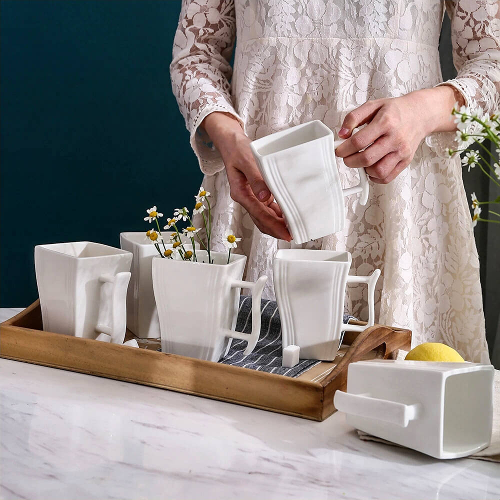 Woman arranging porcelain white mugs on a wooden tray, with flowers and a lemon as decorative accents.