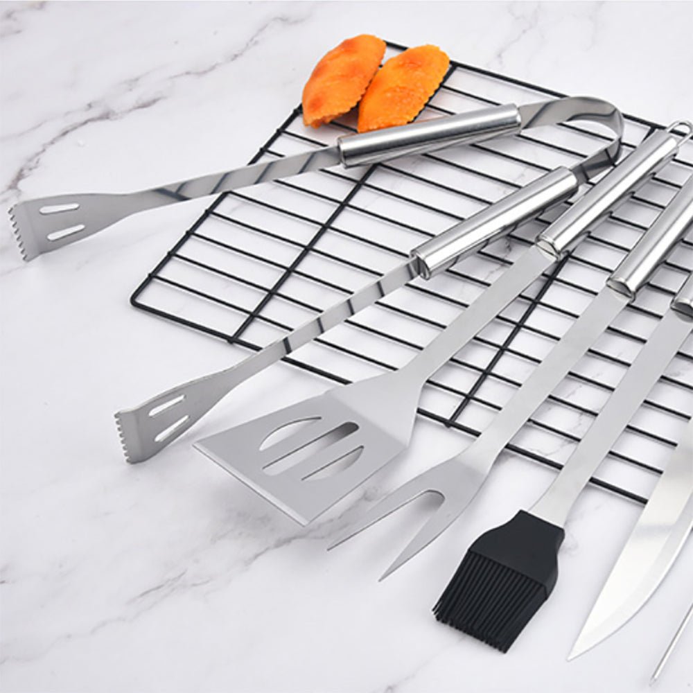 Grill pan with a cooked steak, tongs, a spatula, and a brush beside it, showcasing BBQ tools for grilling.