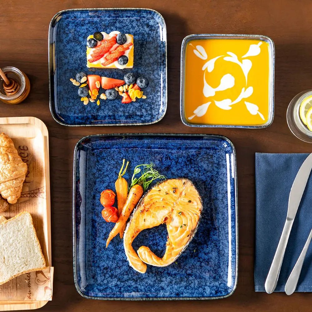 Blue reactive glaze stoneware dinnerware sets with square plates and bowls serving salmon, vegetables, dessert, and soup.
