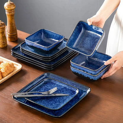 Stacked blue reactive glaze stoneware with square plates and bowls, one bowl held by hand, cutlery placed on top of a plate.