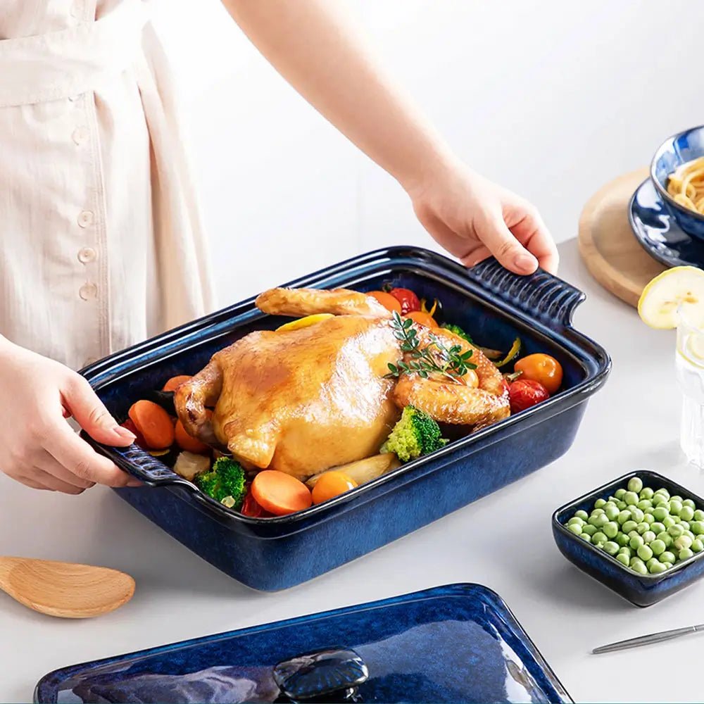 Blue rectangular covered casserole dish filled with roasted chicken, carrots, broccoli, and vegetables, being held by a person at the table.