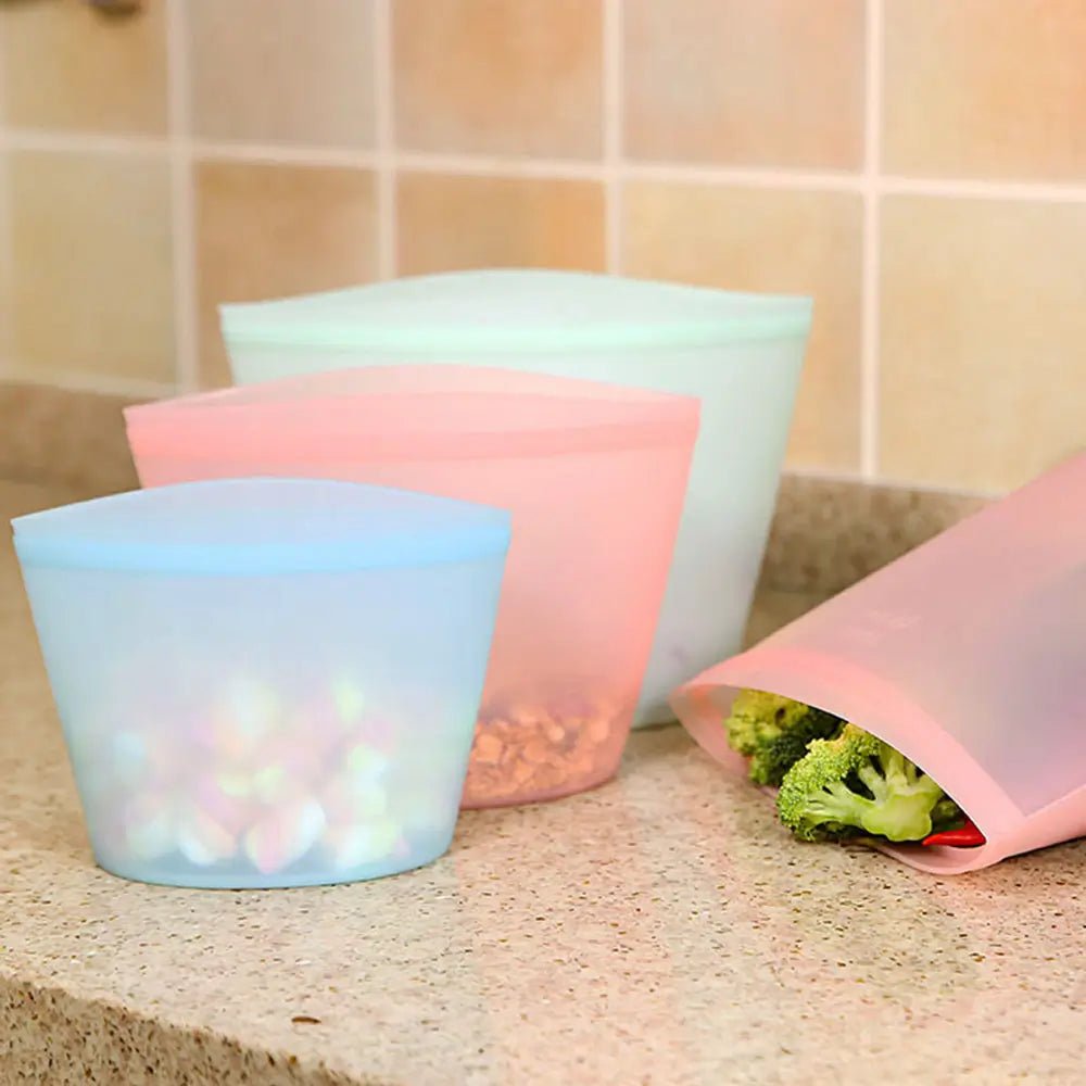 Three brightly colored reusable freezer bags silicone containers, one filled with broccoli, sitting on a kitchen counter.