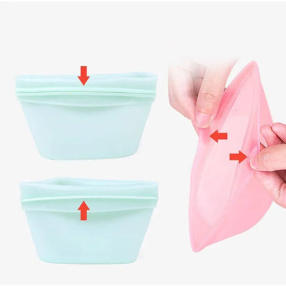 Two light green reusable silicone food bags with red arrows indicating the opening/closing mechanism, and a pink bag being held open by hands.
