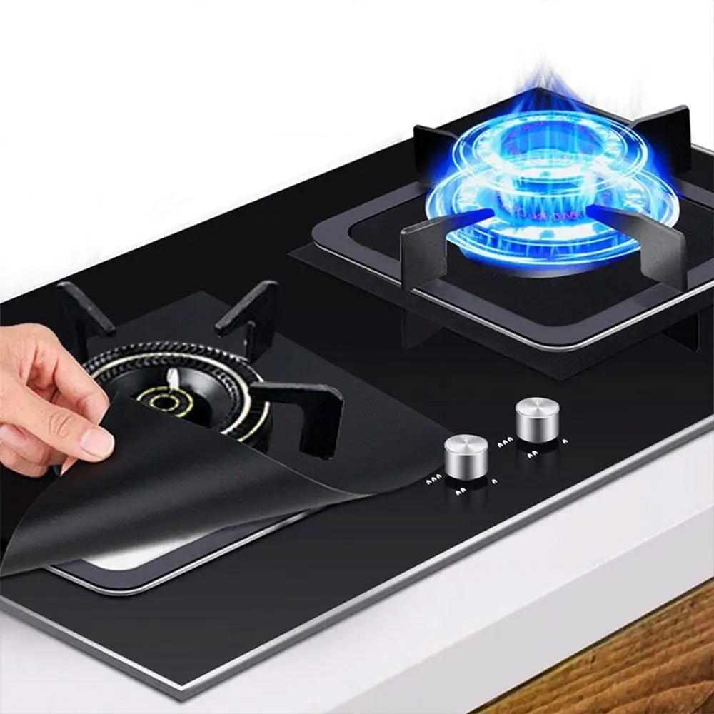 Hand lifting a reusable stove top protector from a gas burner on a black glass stove.