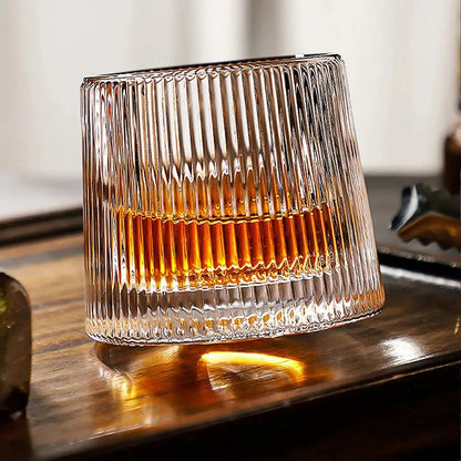 Ribbed-glasses tumbler with vertical ridges holding amber liquid on a wooden surface with light reflections.