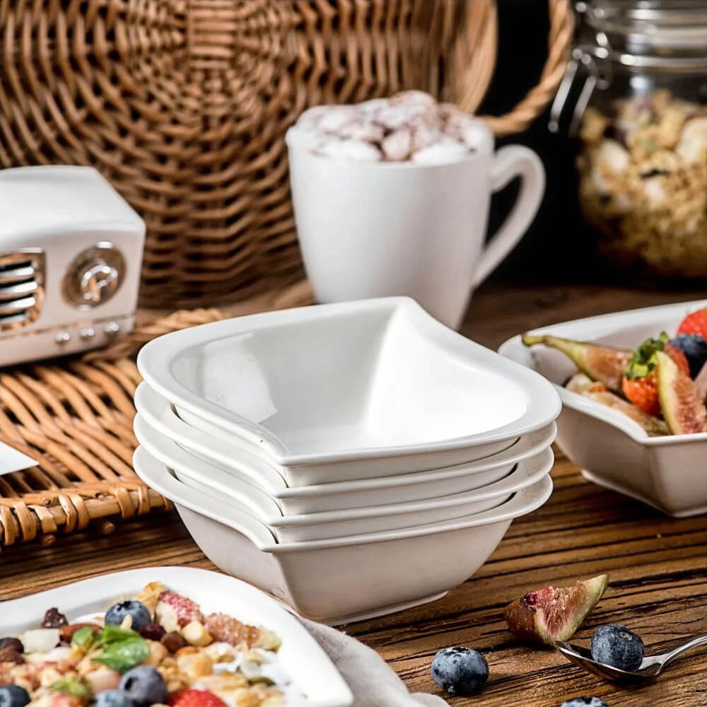 Stack of elegant white serving bowls with a square design, ideal for serving cereals, salads, or desserts, displayed on a rustic wooden table with cozy breakfast settings.