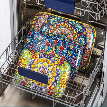Colorful ceramic serving plates with floral and geometric patterns placed inside a dishwasher rack for cleaning.