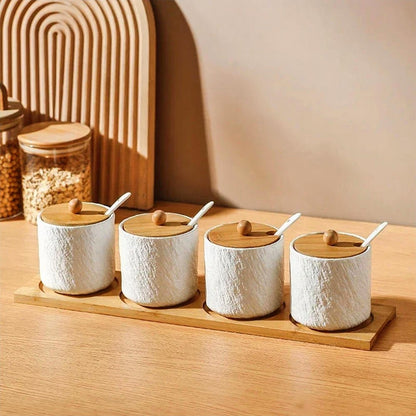 A set of 4 white ceramic kitchen canisters with a textured finish, bamboo lids, and white spoons, neatly placed on a bamboo tray. The background features a wooden arch decor and glass jars filled with grains on a warm wooden countertop, creating a cozy, minimalist kitchen vibe.