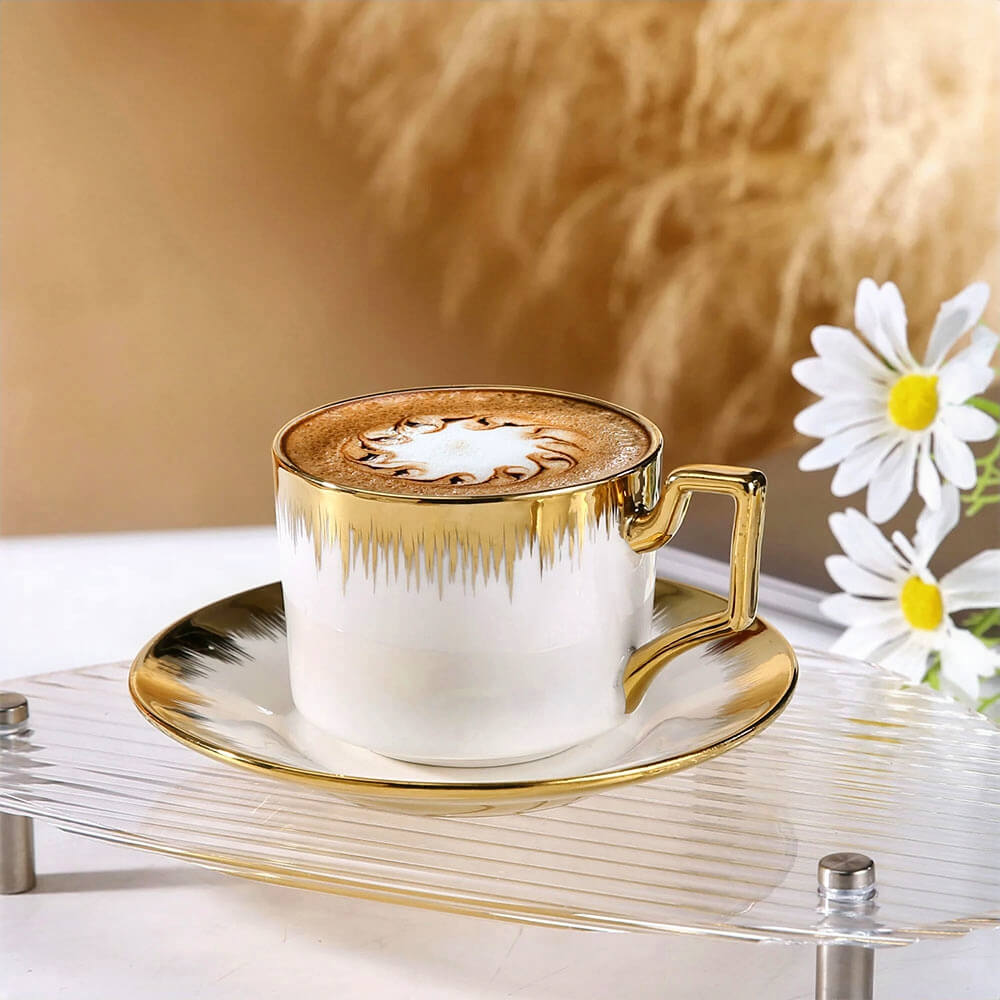 Set of tea cups and saucers with gold accents, featuring elegant porcelain design, latte art coffee, and luxury table setting.