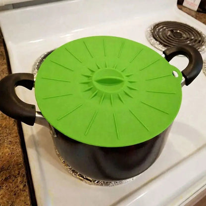 Green silicone cover lid placed on a black cooking pot on a white stovetop, showing a flexible, heat-resistant lid used while cooking.