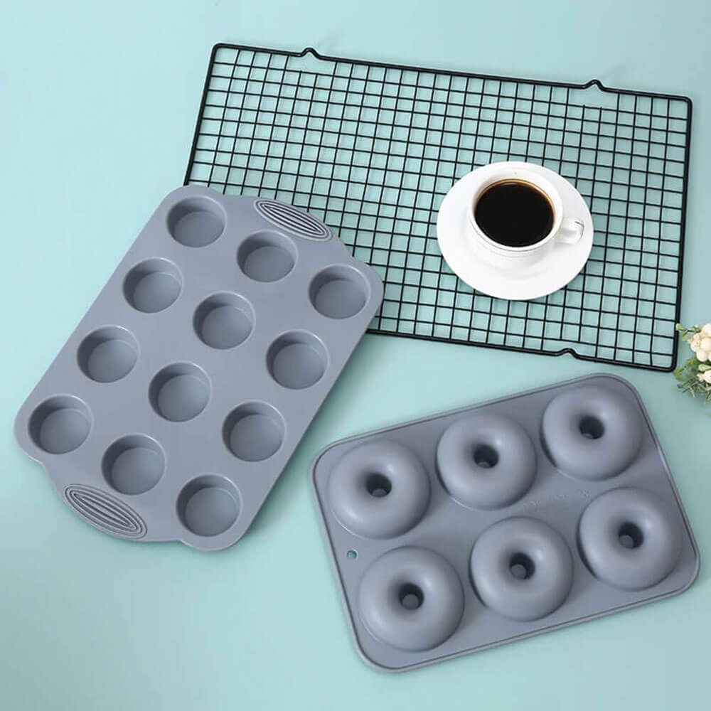 A silicone donut pan set featuring a six-cavity donut pan and a twelve-cavity muffin pan in a sleek gray design. The durable, non-stick silicone ensures effortless release and even baking. The set is shown with a cooling rack, coffee cup, and a mint-green background, highlighting its versatility for creating delicious baked treats at home.