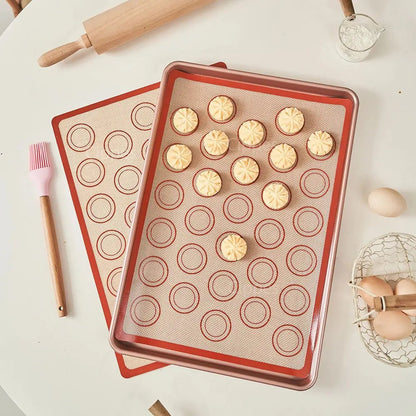 Silicone baking mats with macaron shells on a white surface with baking tools.