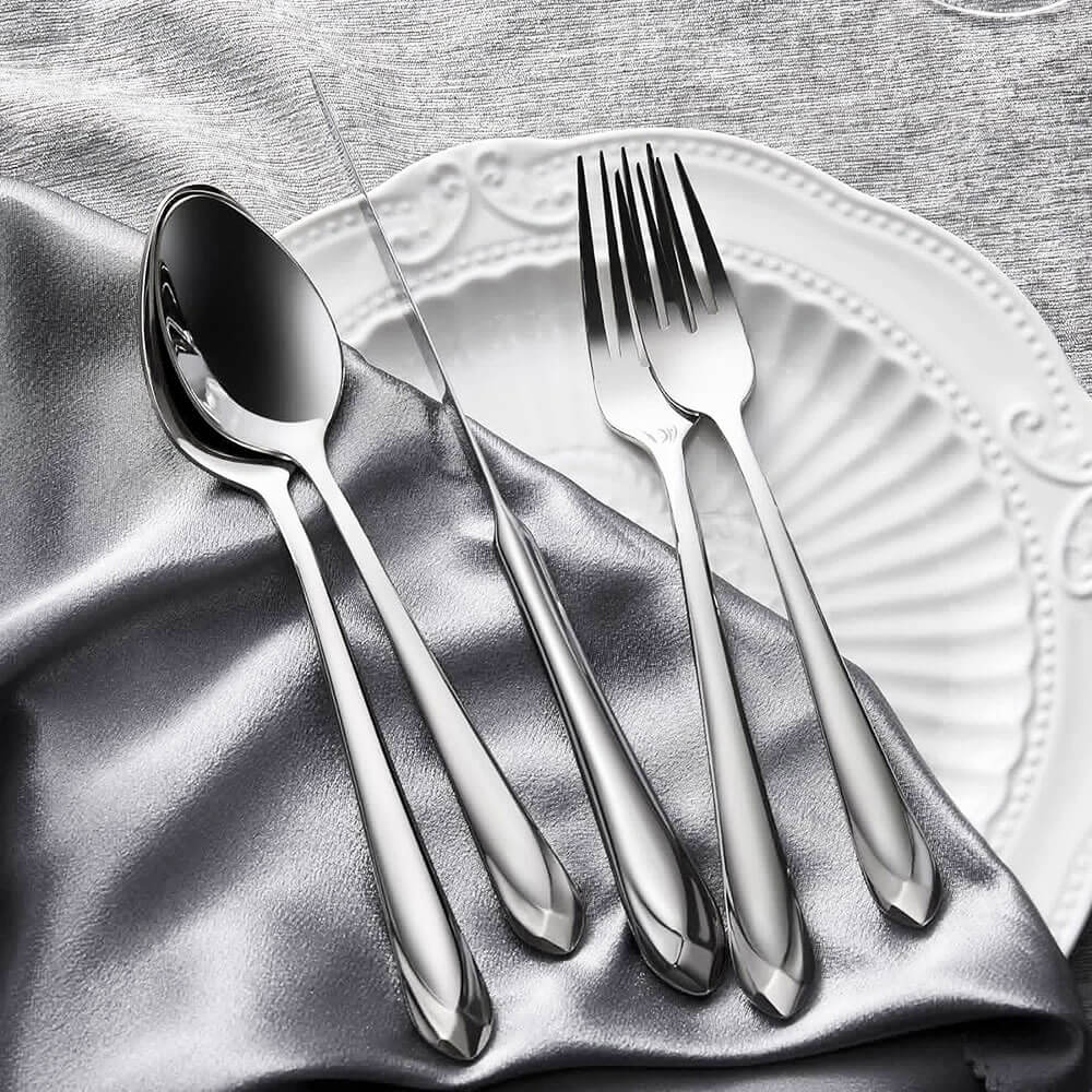 Shiny silverware set 18 10 stainless steel arranged on a white plate with gray satin fabric.