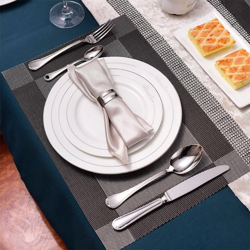 Stainless steel silverware set on a dining table, featuring a dinner fork, dinner knife, soup spoon, and teaspoon.