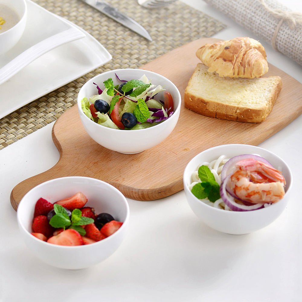 Three snacking bowls: one with fresh strawberries, another with noodles, and the third with salad and olives.