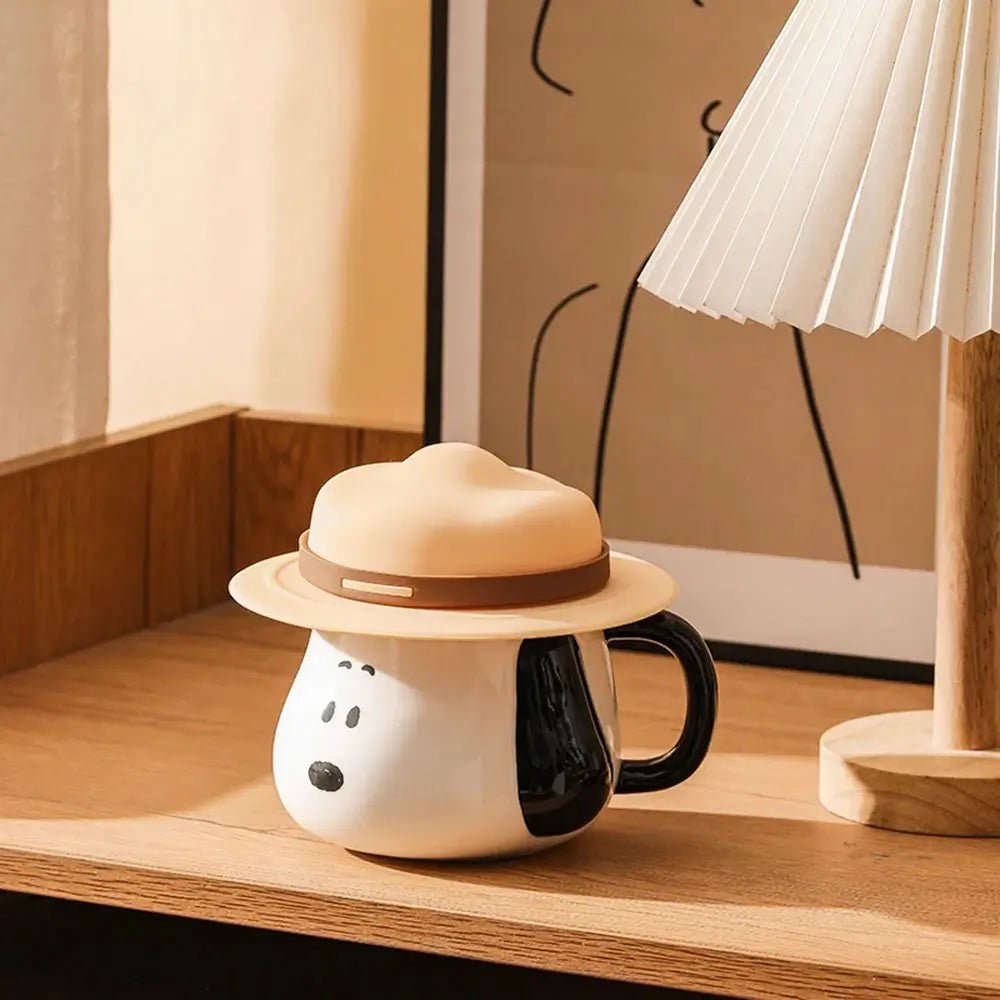 Snoopy coffee mug with a hat on a wooden surface next to a lamp.