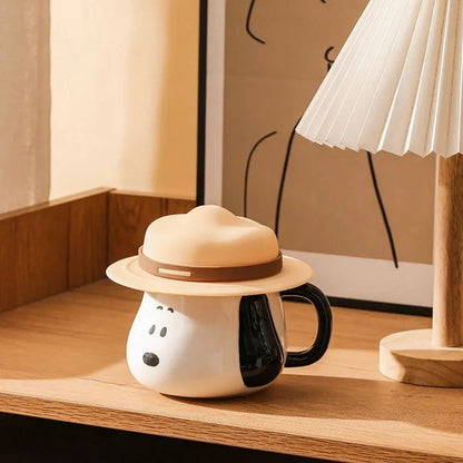 Snoopy coffee mug with a hat on a wooden surface next to a lamp.