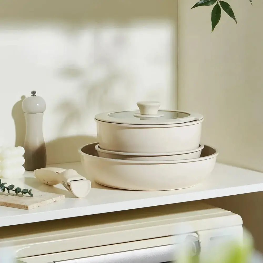 Stackable pans removable handles set shown on a kitchen shelf, including two pans, a glass lid, and a detachable handle beside them.