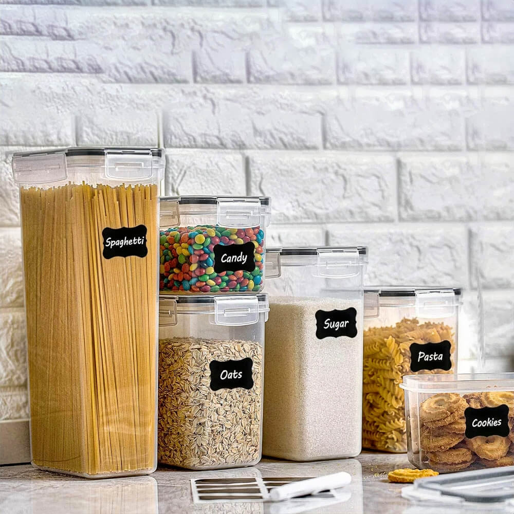 Clear stackable pantry storage containers filled with spaghetti, candy, oats, sugar, pasta, and cookies, labeled for easy organization.