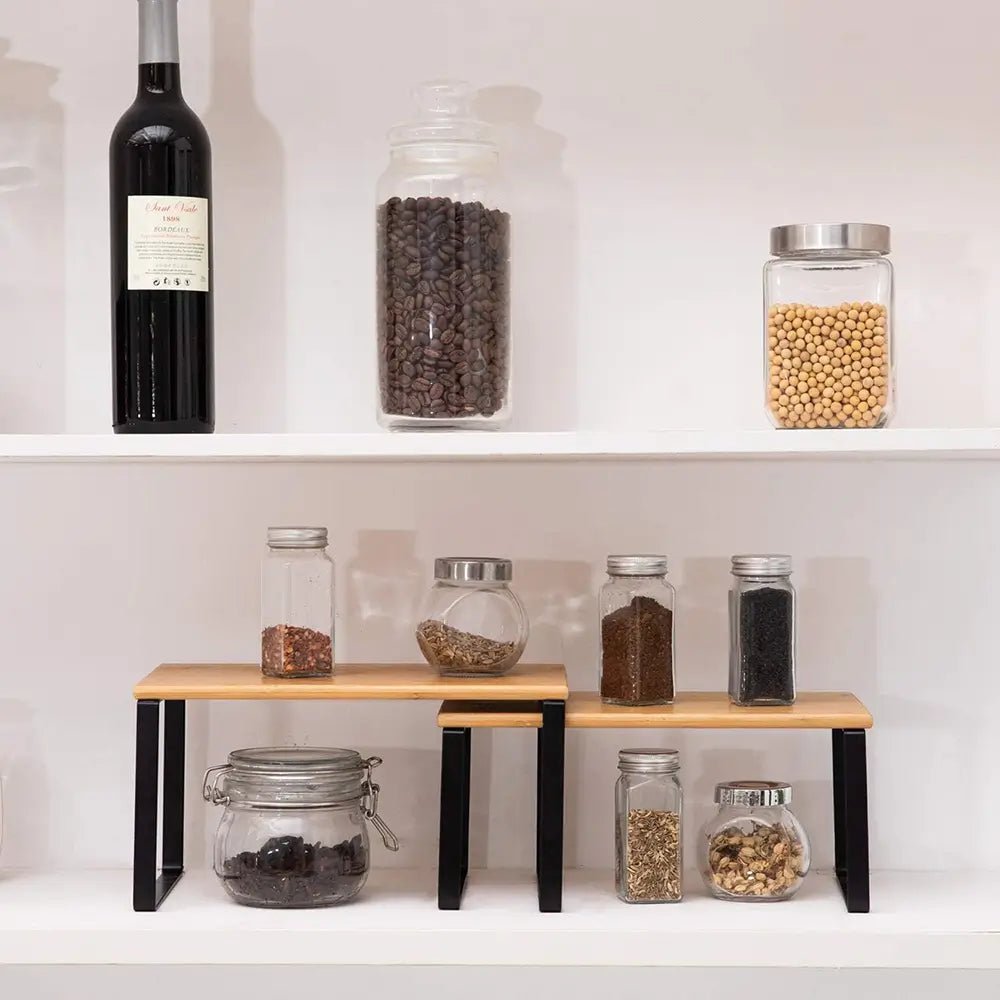 Stackable rack for kitchen holding glass jars with spices and dry goods on a white shelf.