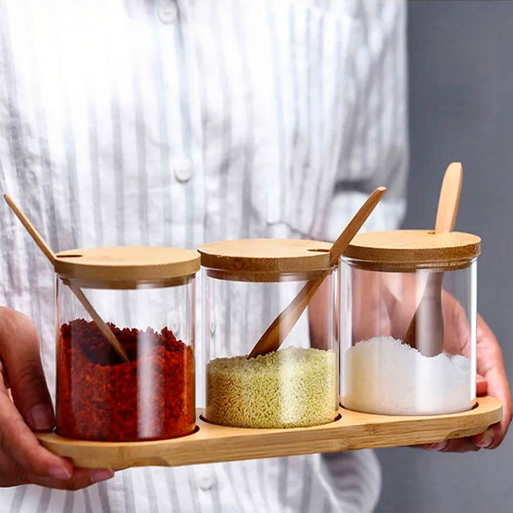 Three stacked tea, coffee, and sugar canisters with see-through glass, bamboo lids, wooden spoons, and a wooden tray, ideal for organized kitchen storage.