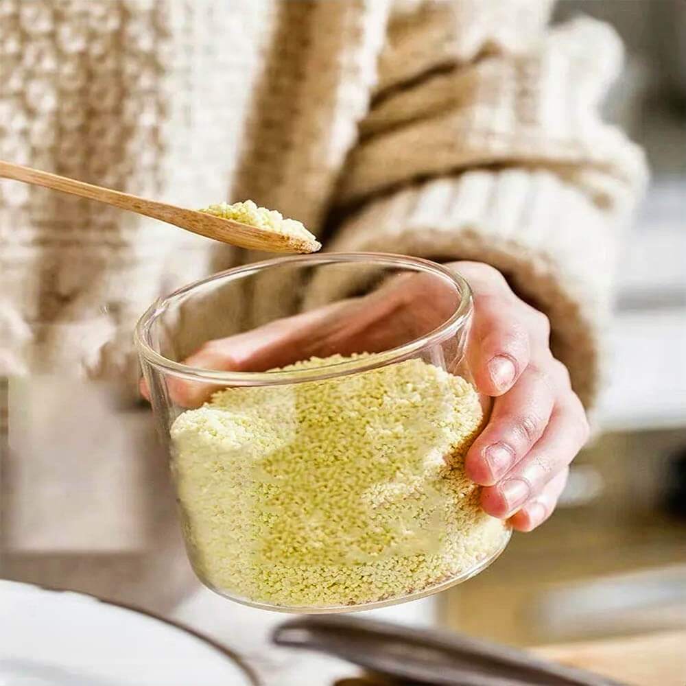 Hand-holding a glass jar from a stacking canister set featuring a bamboo lid and matching wooden spoon, ideal for storing spices, sugar, or grains.