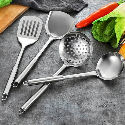 A set of stainless steel cooking utensils arranged on a gray countertop, including a slotted turner, wok spatula, slotted spoon, and ladle. Each utensil features a polished stainless steel finish, smooth ergonomic handles, and hanging loops for easy storage. Fresh vegetables, such as lettuce, peppers, and corn, surround the utensils, adding a vibrant and practical culinary context. This set is ideal for versatile cooking and serving needs.