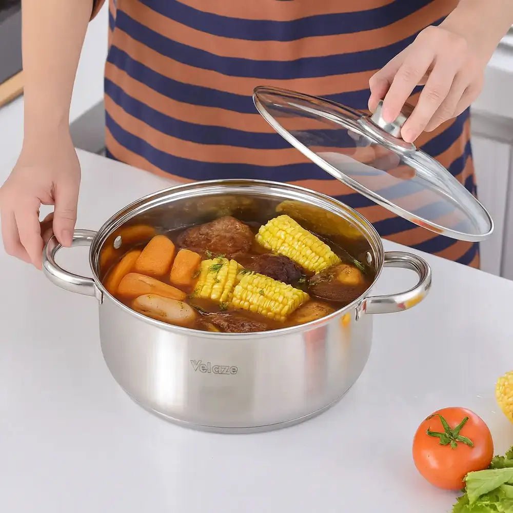 A stainless steel stockpot with glass lid containing corn, carrots, potatoes, and meat on a kitchen counter.