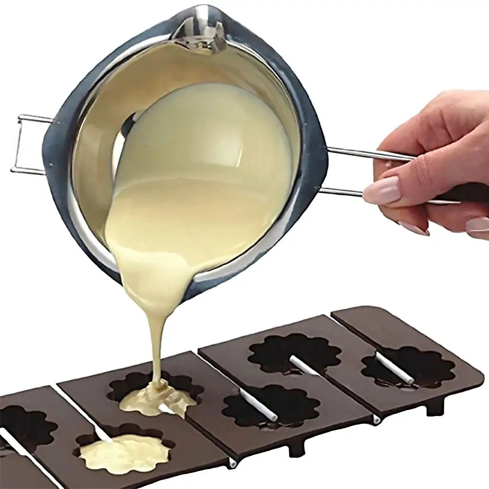 Stainless steel double boiler pot pouring melted white chocolate into silicone molds.
