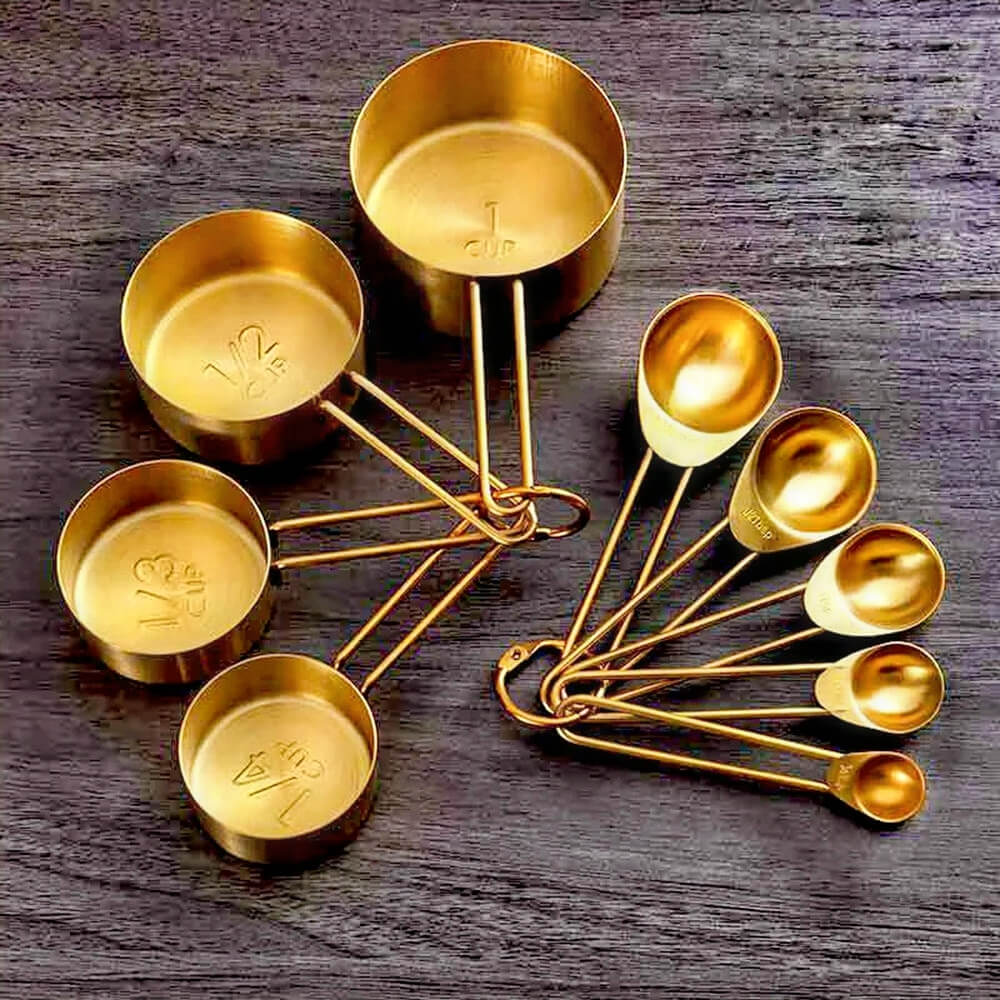 A stunning set of stainless steel measuring cups and spoons with a luxurious gold finish displayed on a dark wooden surface. The set includes precisely labeled measuring cups and spoons, designed for accuracy and style. Perfect for any kitchen, this set combines elegance with practicality, making it a must-have for cooking and baking enthusiasts.