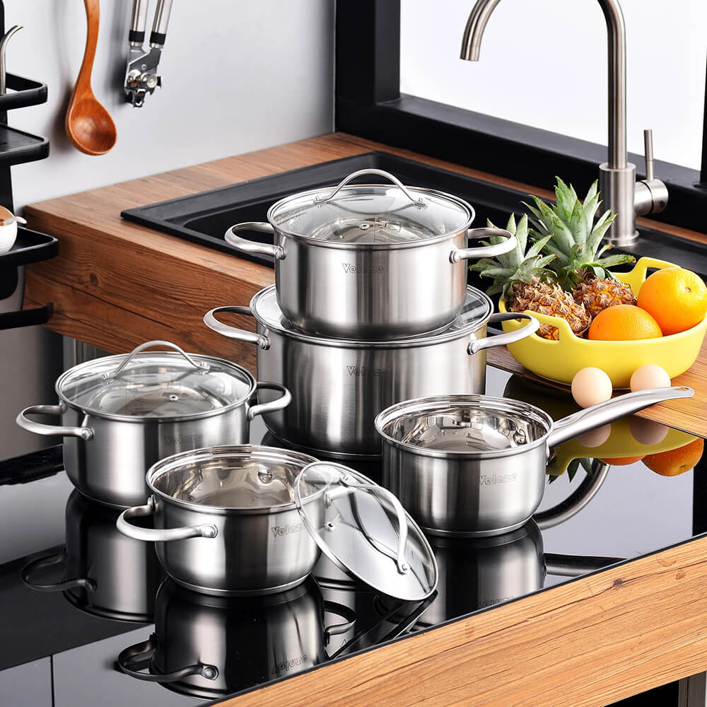 Elegant stainless steel non-stick cookware sets are displayed in a modern kitchen, featuring multiple pots and pans with glass lids, ideal for versatile cooking.