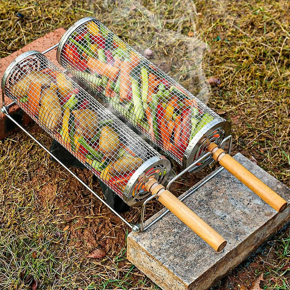 Two stainless steel rolling BBQ grill baskets with wooden handles, filled with veggies, cooking over outdoor fire.