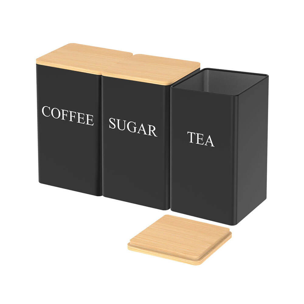 Set of three black stainless steel storage containers labeled COFFEE, SUGAR, and TEA, with bamboo lids and one lid placed separately.