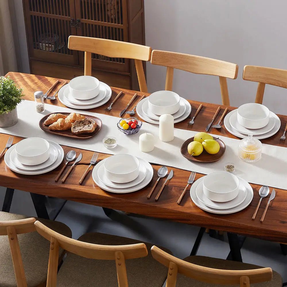 Dining table set with white ceramic plates, bowls, and cutlery on a wooden table.