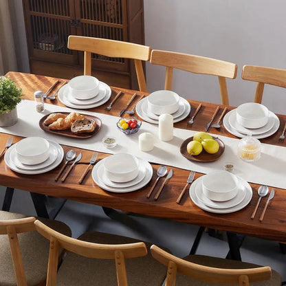 Dining table set with white ceramic plates, bowls, and cutlery on a wooden table.