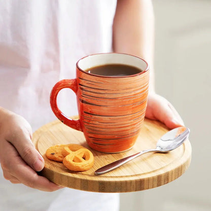 Person holding a wooden tray with an orange mug of coffee, cookies, and a spoon.