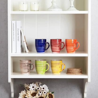 A set of six colorful stoneware mugs displayed on a white shelf, featuring red, blue, orange, beige, green, and yellow finishes.