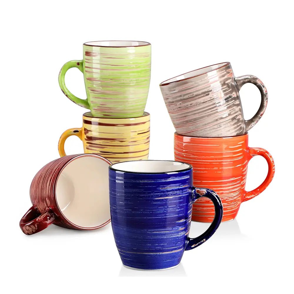 A collection of colorful stoneware mugs with ribbed textured glaze in red, blue, green, yellow, orange, and beige, stacked together on a white surface.