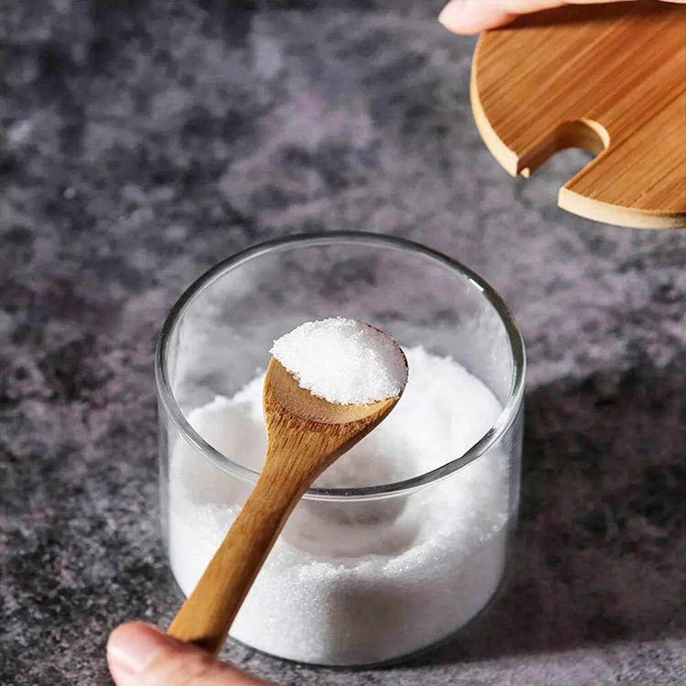 Close-up of a glass jar from a tea coffee sugar canisters stack, featuring a bamboo lid and wooden spoon, perfect for keeping kitchen essentials fresh.