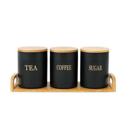 Tea coffee sugar canisters in matte black with bamboo lids, arranged on a wooden tray against a white background.