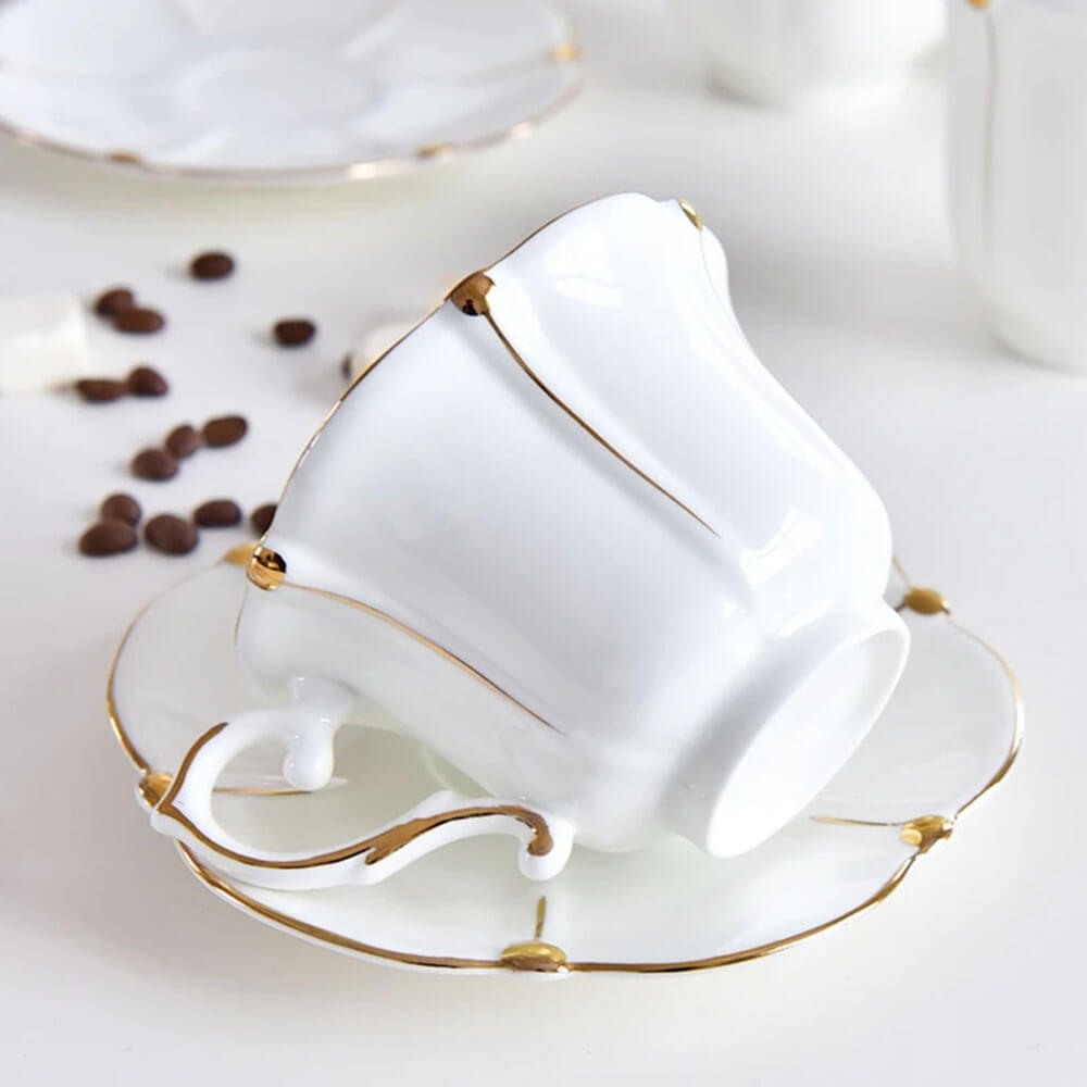 Elegant white teacup with gold accents resting on a matching saucer, part of a sophisticated tea set for adults, perfect for refined tea gatherings.