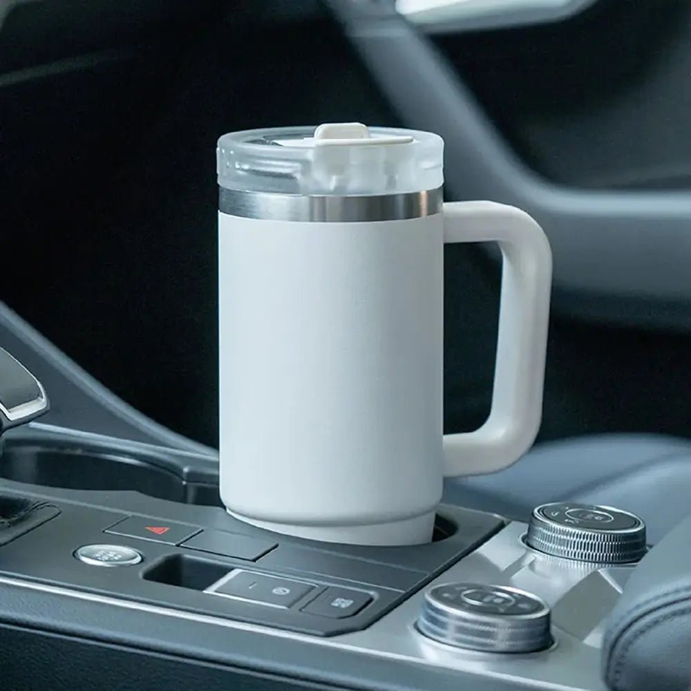 White TYESO thermal coffee travel mug with handle and clear lid placed in a car cup holder.