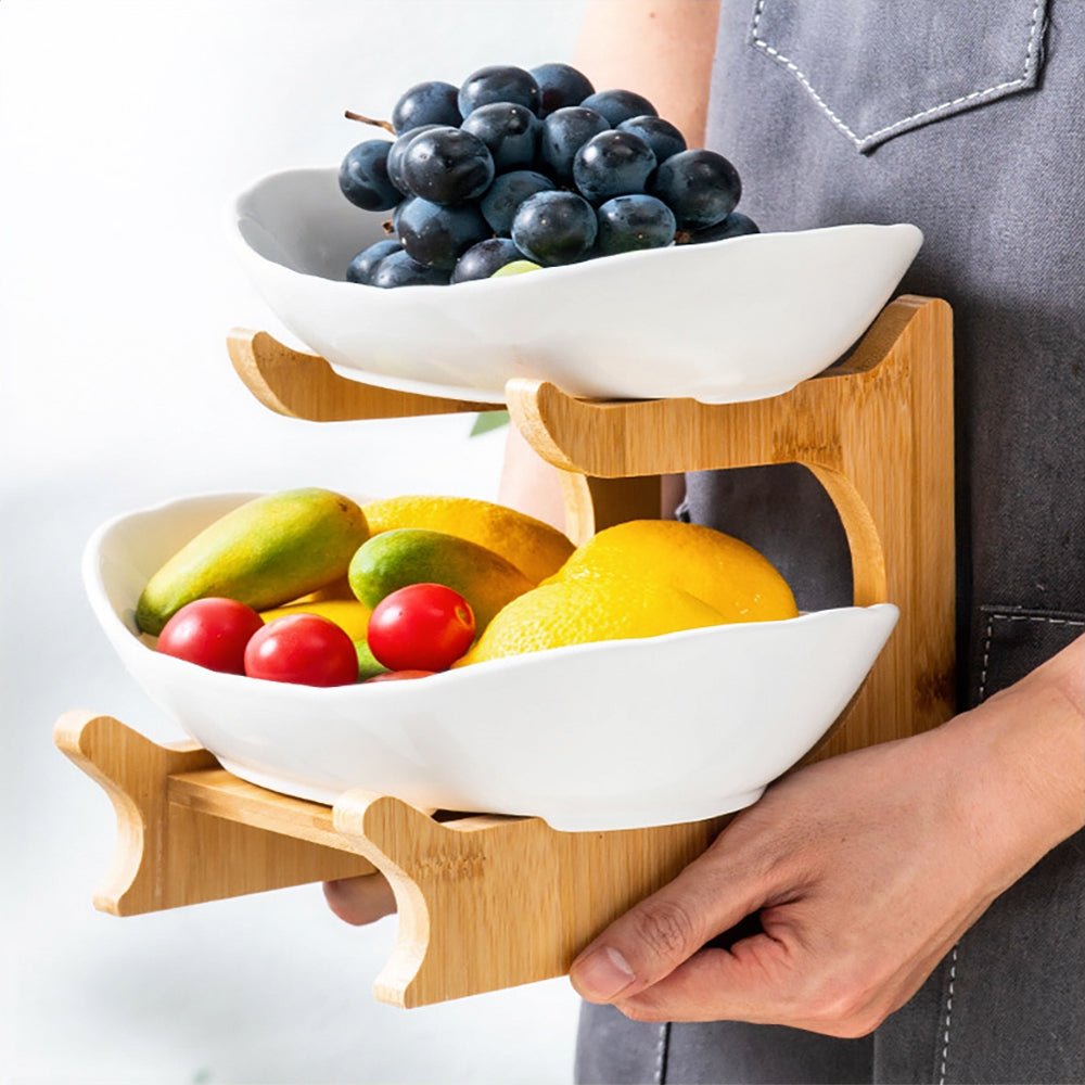 A woman holding a white tiered fruit bowl filled with a variety of fresh fruits, showcasing its elegant design and ample space for serving or displaying produce.