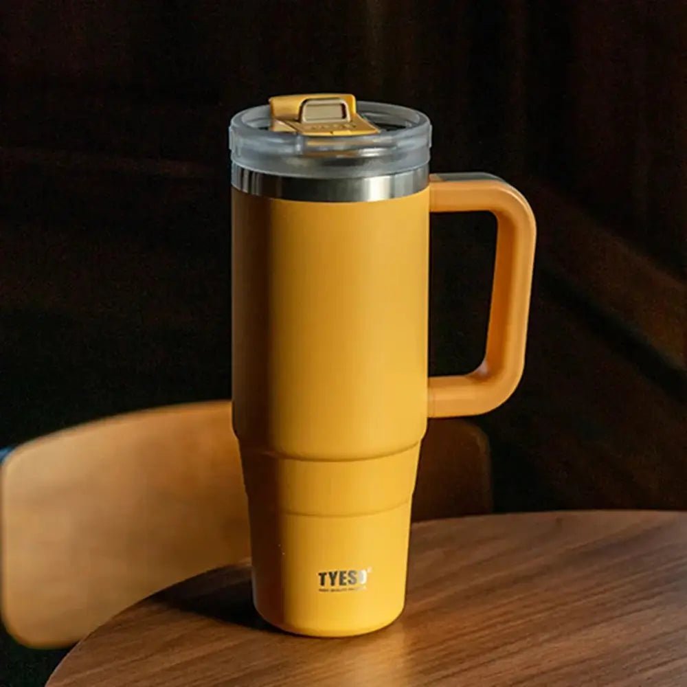 Yellow travel thermal mug with handle on a wooden surface against a dark background.