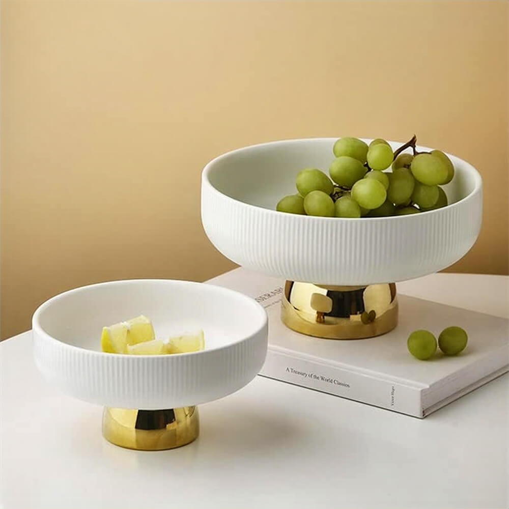 White ceramic pedestal fruit bowl with a gold foot, filled with fresh grapes, adding elegance to any setting.