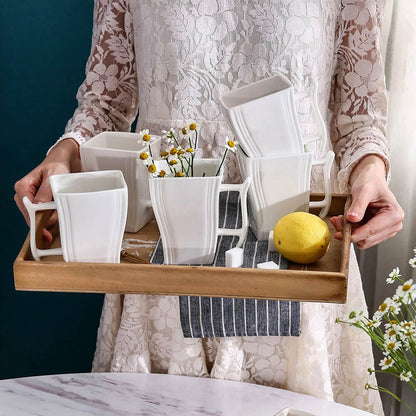 Woman holding a wooden tray with elegant white porcelain mugs, decorated with flowers and a lemon for style.