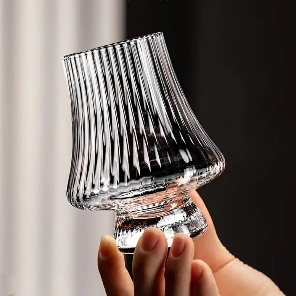 Clear ribbed crystal wine tasting glasses with a flared bowl and sturdy base, shown being held by hand against a softly lit background.