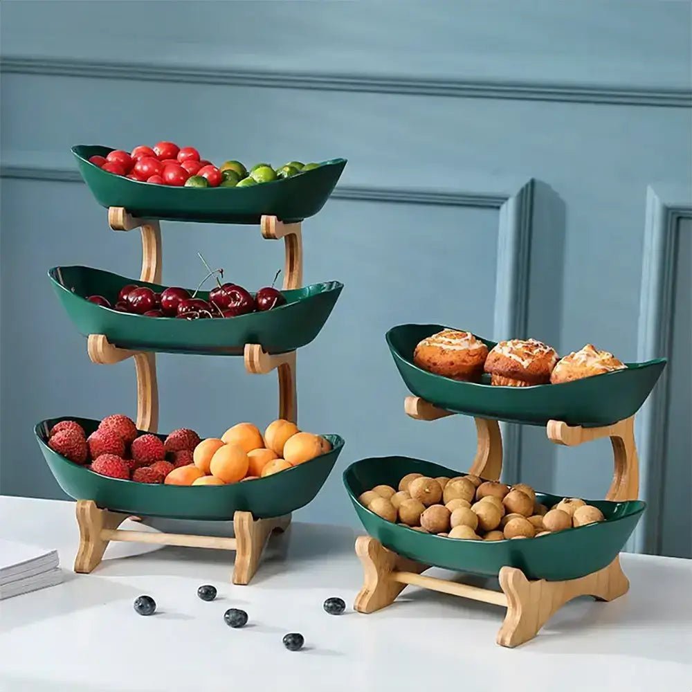 Two-tiered and three-tiered wooden stands holding green ceramic bowls filled with lychees, cherries, citrus fruits, muffins, and longan fruits.